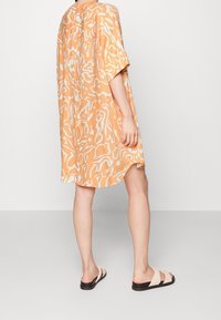 Abito oversize a maniche corte di colore arancione con motivi astratti bianchi, realizzato in un tessuto leggero. Presenta un orlo curvo e una vestibilità rilassata.