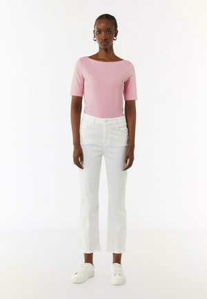 Roze T-shirt met korte mouwen gecombineerd met witte rechte broek en witte sneakers. De outfit heeft een eenvoudig, strak ontwerp en effen kleuren.