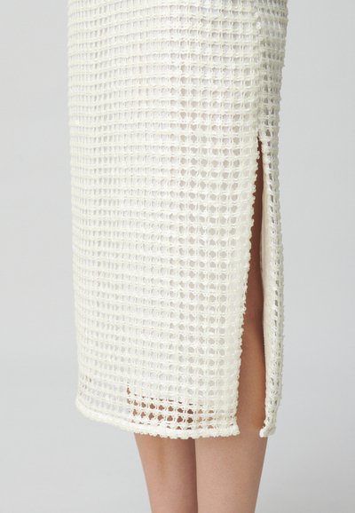 Jupe tissée blanche avec un motif en maille ouverte, de longueur mi-longue avec une fente sur le côté, et une finition texturée le long de l'ourlet.