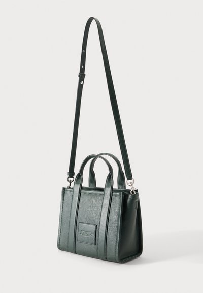 Sac à main en cuir texturé vert foncé avec deux poignées supérieures et une longue bandoulière réglable, debout sur un fond uni.