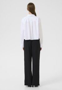 Biała, wykładana, krótka koszula z długimi rękawami, w połączeniu z luźnymi, czarnymi spodniami. Gładki materiał i dopasowany fason.