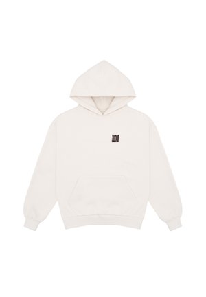 Personne portant un sweat à capuche blanc avec un texte noir et un pantalon marron, vue de dos sur un fond gris uni.