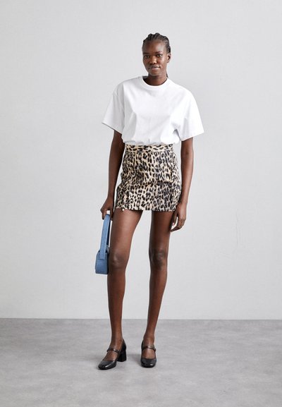 Hvit oversized t-skjorte, leopardmønster mini skjørt, svarte høye sko og en blå håndveske. Stoffet virker mykt med et dyremønster.