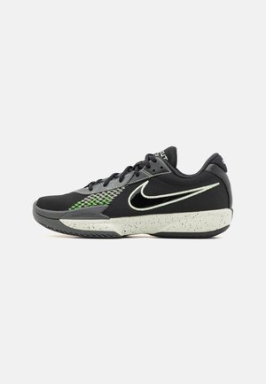 Sort og grå Nike sportssko med hvid plettet sål, sorte snørebånd, neon grønne accenter og stort hvidt swoosh-logo på siden.
