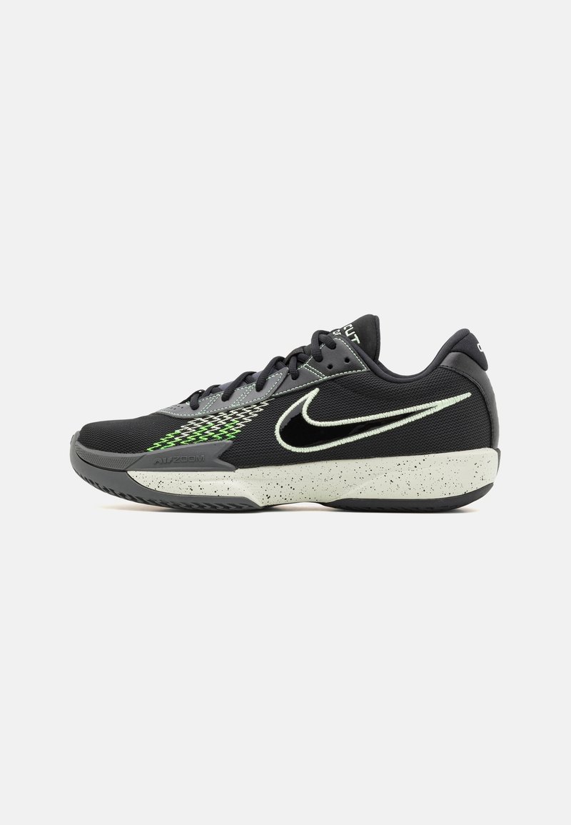 Chaussure de sport Nike noire et grise avec semelle blanche mouchetée, lacets noirs, accents vert néon et grand logo Swoosh blanc sur le côté.