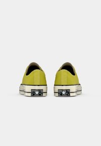 Tenisi din pânză verde lime cu un design cu tăietură joasă și accente din cauciuc negru, având o talpă clasică din cauciuc alb și brandul Converse pe spate.