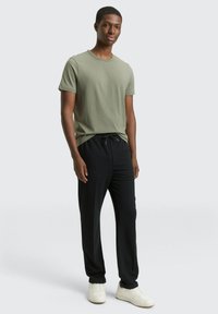 Oliwkowo-zielony t-shirt z krótkim rękawem, zestawiony z czarnymi spodniami na sznurku i białymi trampkami; gładka tkanina i swobodny krój.