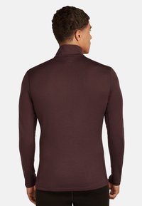 Camisa de manga larga de tejido burdeos profundo, con un cuello alto y un diseño ajustado. Textura suave sin patrones o acentos visibles.