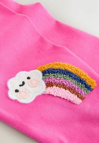 Różowy materiał z haftowaną uśmiechniętą chmurką z brzoskwiniowymi policzkami, obok tęczy z teksturowanych, wielokolorowych nitek.