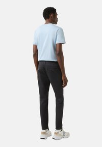 Hellblaues kurzärmliges T-Shirt, schwarze Hose und weiße Turnschuhe mit beigen Akzenten; schlichtes, tailliertes Design, sichtbare Nähte.