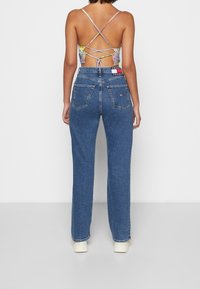 Jeans de mezclilla azul de pierna recta con una cintura alta, que cuentan con bolsillos traseros y una etiqueta de la marca. La tela tiene una textura suave y ligeramente descolorida.