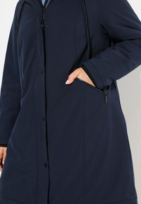 Navy blue long jacket made of smooth fabric, featuring a zippered pocket, snap buttons, and a drawstring hood.