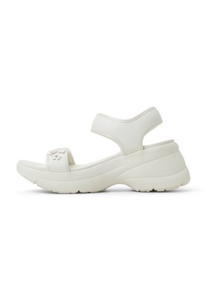 Sandalias blancas de cuña con un upper sintético suave, correas ajustables, adornos florales y una suela de goma texturizada para agarre.