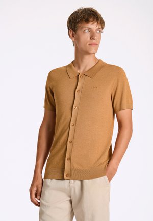 Polo à manches courtes de couleur moutarde en tissu doux, avec un devant boutonné et un ourlet côtelé, arborant un logo brodé.