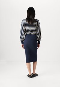 Jupe crayon marine avec une coupe ajustée, associée à un haut à rayures horizontales à manches longues en marine et crème. Portée avec des chaussures plates noires.