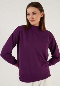 Felpa lunga viola con maniche lunghe, collo alto e polsini a costine, realizzata in tessuto morbido, caratterizzata da una vestibilità comoda e dettagli minimi.
