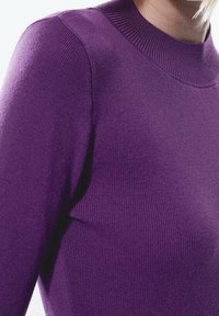 Maglione a coste viola con colletto alto, caratterizzato da un tessuto liscio e texturizzato e una silhouette aderente, che mette in evidenza i dettagli delle cuciture delle maniche.