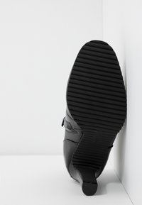 Zapato de cuero negro con tacón bajo, que cuenta con una suela de caucho texturizada con estrías y un cierre de cremallera lateral.