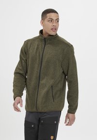 Olivengrön fleecejacka med hög krage, dragkedja fram och två sidofickor. Tyget har en strukturerad yta med subtila mönster.