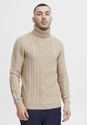 Suéter de punto beige con cuello alto, que presenta un diseño de trenzas, puños acanalados y dobladillos. Textura suave con un diseño ajustado.