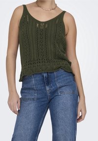 Olive green knitted tank top with a scalloped hem, featuring vertical ribbing and openwork patterns. Paired with high-waisted blue jeans.