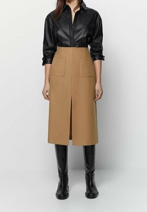 Sort læder skjorte med knaplukning parret med en knælang kamelfarvet nederdel med to frontlommer og en frontslids, suppleret af sorte støvler.