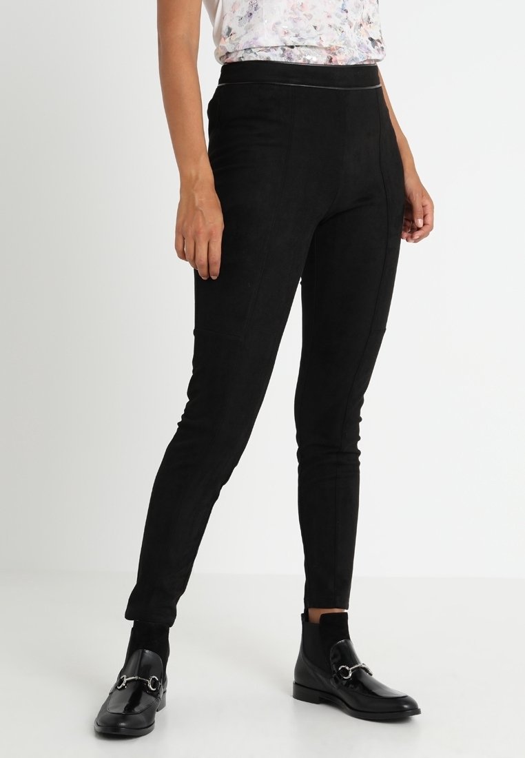 Pantalons en suede noir avec une coupe slim, dotés de détails cousus et d'une taille élastique. Associés à des bottines noires et un top fleuri.