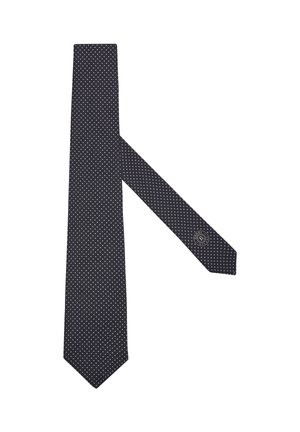 Corbata negra con pequeños lunares blancos y un logo circular cerca del extremo estrecho sobre un fondo blanco.