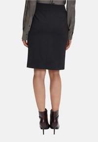 Svart blyertsskjol med rak skärning, med slits bak och dold dragkedja, kombinerad med bruna ankelskor, visad bakifrån.