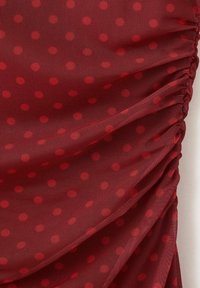 Tissu rouge transparent avec de petits pois rouges, froncé et plissé le long du côté droit.