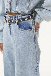 Veste en denim bleu clair et jean, avec une coupe décontractée, des détails de couture visibles et une ceinture en cuir noire avec des clous en argent.