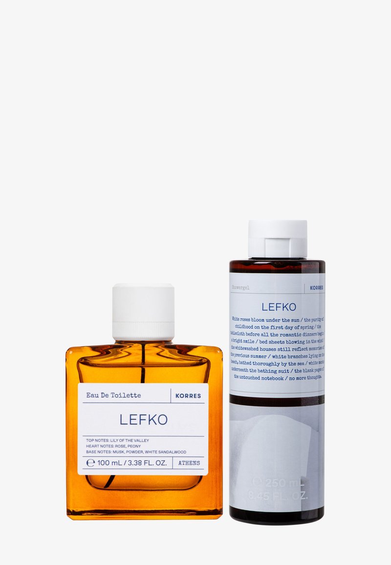 Bursztynowa szklana butelka Korres Lefko Eau de Toilette (100 ml) obok ciemnobrązowej butelki żelu pod prysznic (250 ml). Obie mają białe etykiety i zakrętki.