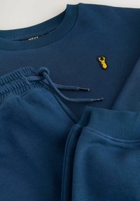 Mørkeblå sweatshirt med ribbestrikket halsudskæring og broderet gult hjortelogo; matchende joggers har elastisk vælg med snøre.