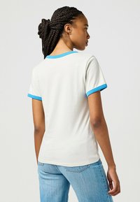 Camiseta de manga corta en crema claro con cuello y dobladillo de las mangas de rayas azules, con un tejido suave y un corte clásico.