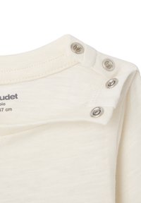 Nahaufnahme des cremefarbenen Babyhemds am Halsausschnitt mit drei metallenen Druckknöpfen, die an einer Schulter teilweise geöffnet sind.