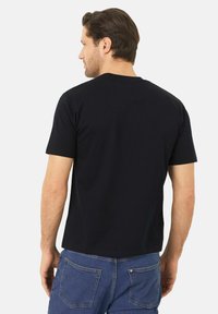 Černé bavlněné tričko s krátkým rukávem, kulatým výstřihem a rovného střihu. Nosené s modrými džíny, zobrazený jednoduchý pohled zezadu.