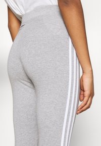 Grå leggings tillverkade av en blandning av bomull, med hög midja och vita randiga detaljer längs sidorna. Slät textur och figurnära passform.