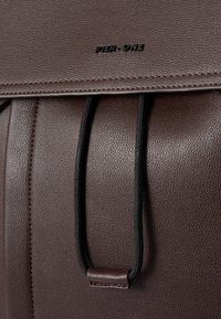 Bolso de cuero sintético texturizado marrón con una correa que presenta acentos elásticos negros y el logo grabado "PIER ONE" en la solapa.