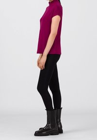 Kortærmet top med høj hals i livlig magenta, parret med sorte skinny bukser og kraftige sorte ankelstøvler, sat mod en ensfarvet baggrund.