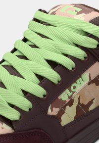 Baskets violettes et marron avec un motif camouflage, des lacets vert vif et le mot "GLOBE" en vert sur le côté. Matériau texturé.