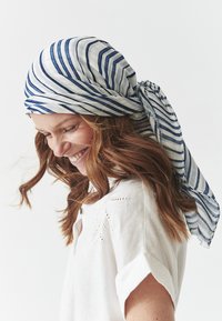 Ribad sinine ja valge sall, mis on valmistatud kergest kangast, seotuna selja taga, ripub elegantselt, täiustades valget särki, millel on detailne õmblemine.