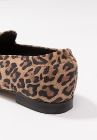 Chaussure plate à imprimé léopard marron et noir avec un talon rond et une semelle noire sur fond blanc.