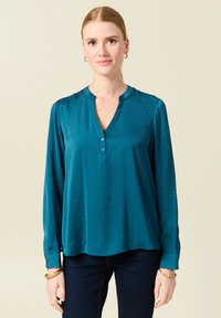 Blusa teal a maniche lunghe realizzata in tessuto liscio con una leggera lucentezza. Presenta una chiusura con bottoni e un colletto arrotondato.