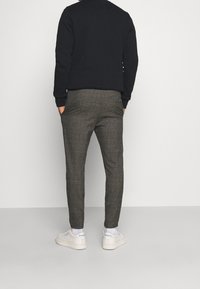 Herre slim-fit bukser i mønstret, brunt tern med lommer. Kombineret med en sort sweatshirt og hvide sneakers.