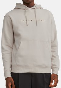 Vaalean beige huppari, jossa on naruilla säädettävä huppu, etutasku ja tummalla tekstillä "JACK & JONES" logo rinnassa. Sileä kangas.