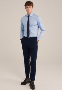 Világoskék ing, terjesztett gallérral, sötét nyakkendővel, tengerészkék nadrággal és fekete cipővel. Slim fit dizájn, sima textúra.