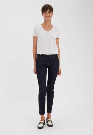 T-shirt blanc à col en V, jean skinny bleu foncé, chaussures à enfiler noires et blanches. Styles simples avec une coupe décontractée, design minimaliste.