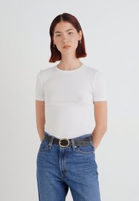 T-shirt blanc à manches courtes avec un col rond, associé à un jean bleu taille haute et une ceinture noire avec une boucle circulaire.