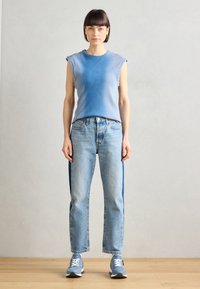 Világoskék, bordázott ujjatlan felső magas derekú kék farmernadrággal, sötétkék oldalsávokkal. A modellen szürke sportcipők vannak.