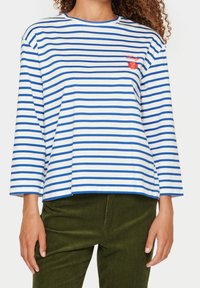 Pasiasta bluzka w białym i niebieskim kolorze, wykonana z bawełny, z rękawami 3/4, z małym czerwonym haftem w kwiaty na piersi.